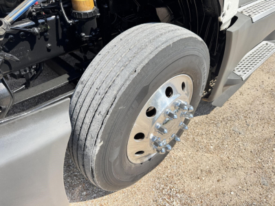 Truck wheel close-up showing front dual rear? solid tire with polished lug nuts and aluminum wheel.