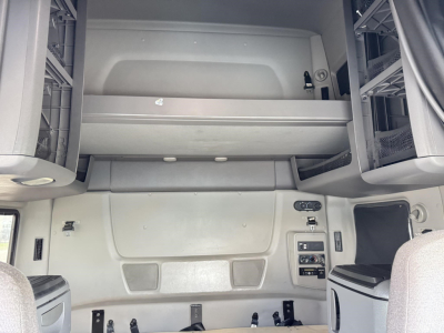 Truck cabin interior showing overhead bunk storage and control panel with switches, seating area, and side storage compartments.