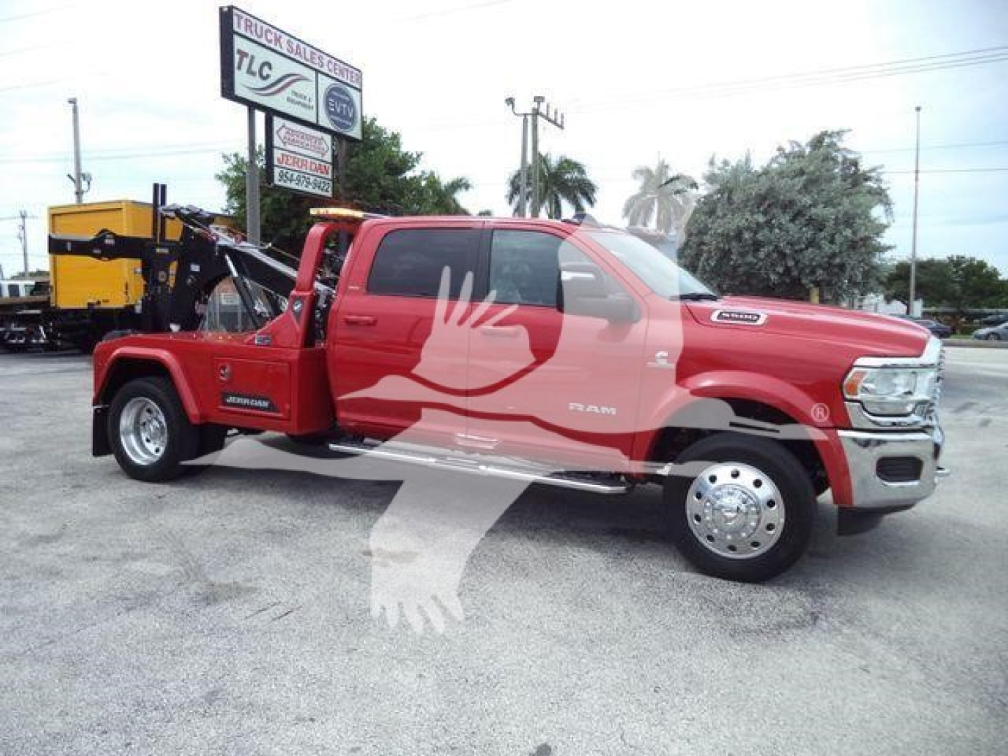 Red Ram truck with a winch bed, side view, orange tow equipment in background. Visible text includes RAM emblem on front fender and logo on door; no other legible details readable.