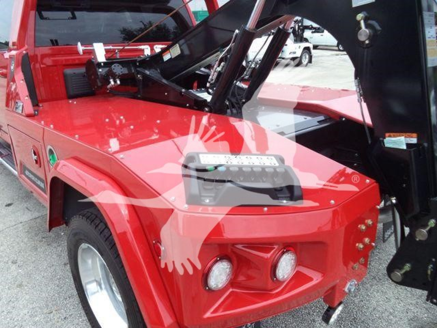 Front end of a red Ram truck with a winch system visible in the bed, headlight cluster, and warning decals.
