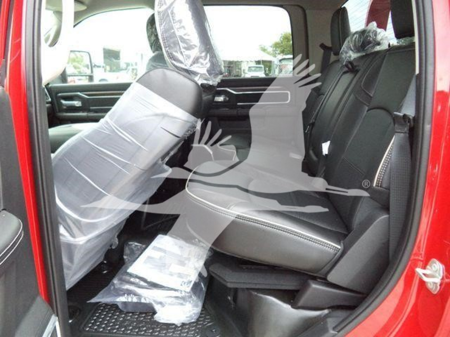 Ram truck interior rear seating with protective plastic on seatbacks and plastic-wrapped front seat, red exterior, showroom setting.