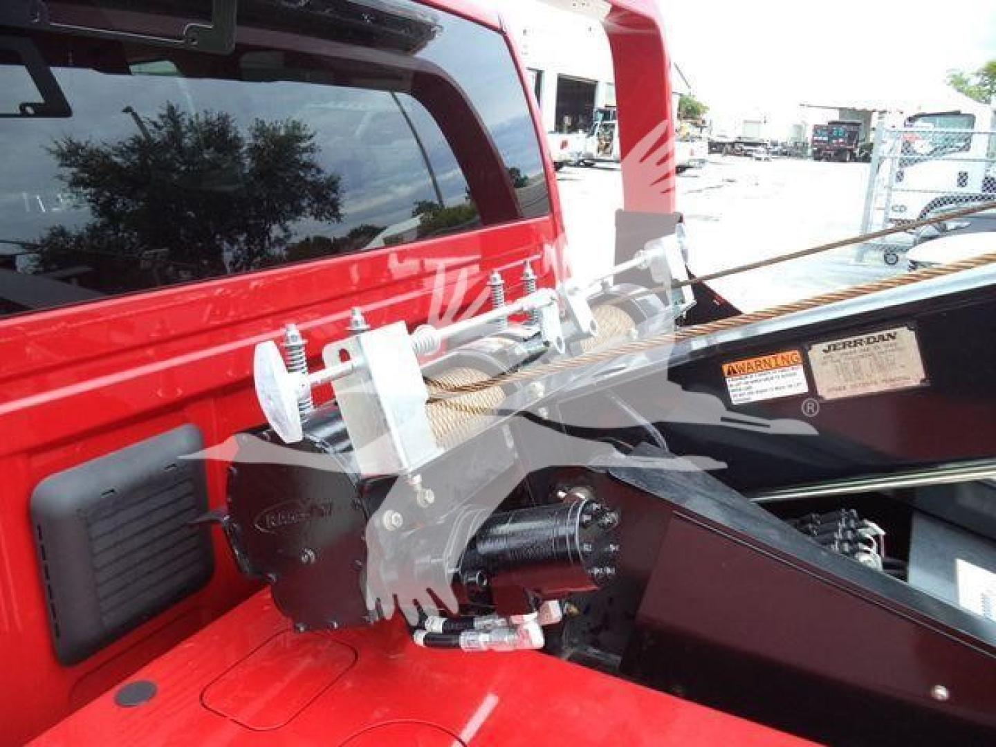 Ram pickup with a mounted winch assembly in the truck bed area. Visible components include a black winch housing, silver fairlead, and hydraulic hoses; red truck body in view.