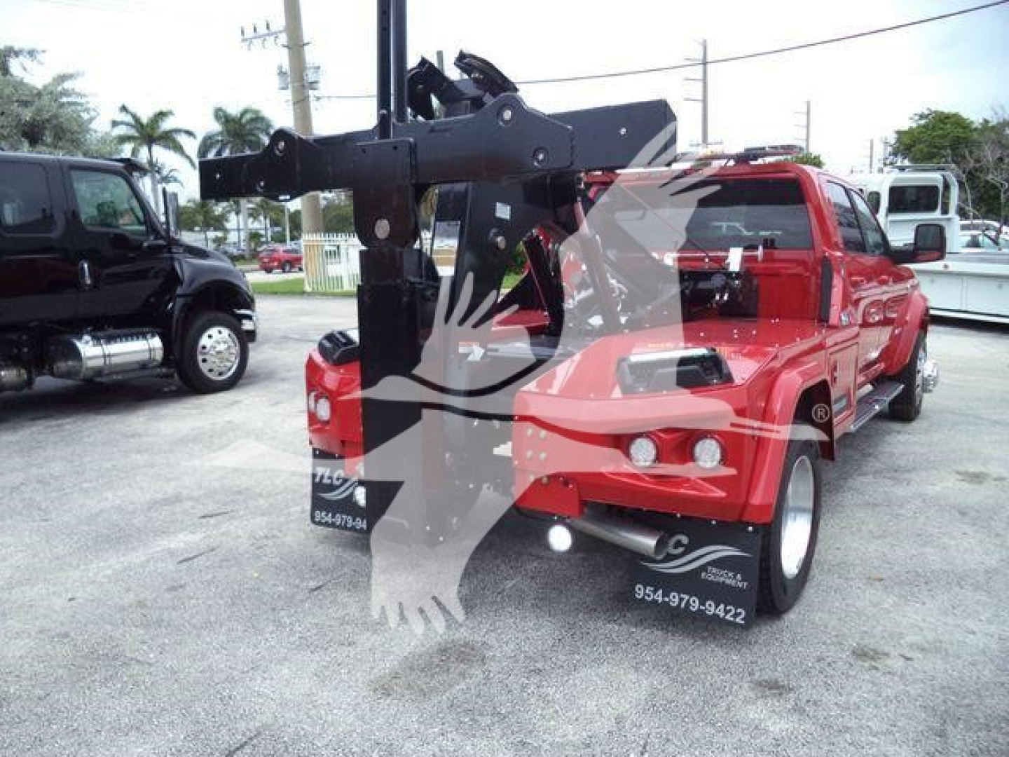 Ram pickup truck with a mounted winch/crane device in red color, rear view showing winch arm and hydraulic assembly, dealership lot in background.