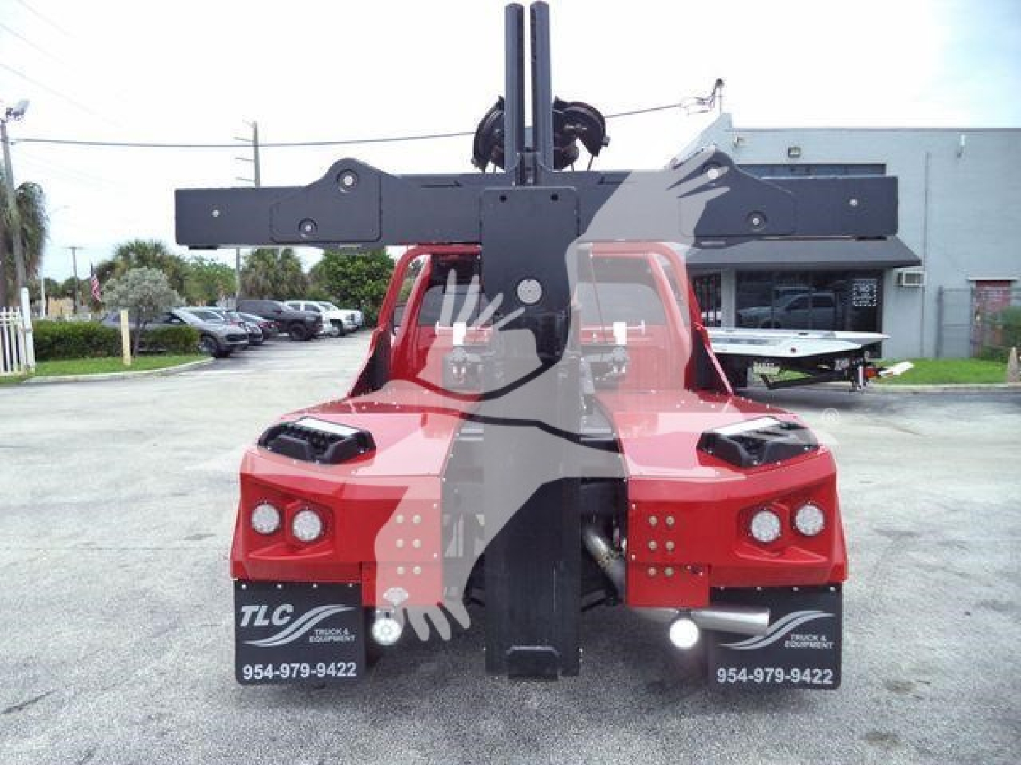 Truck with mounted winch and hitch apparatus on rear, red cab, dealership lot in background, license plate area and TLC branding visible.