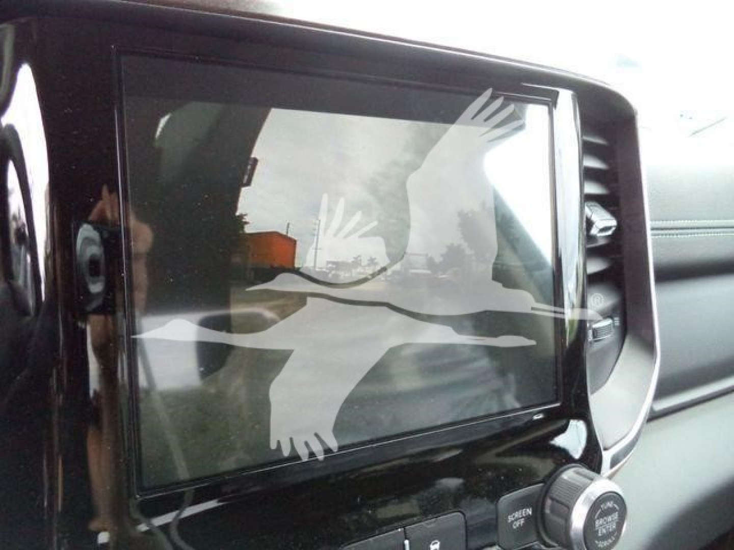 Ram truck interior showing a touchscreen display with reflection of a hand and bird watermark.