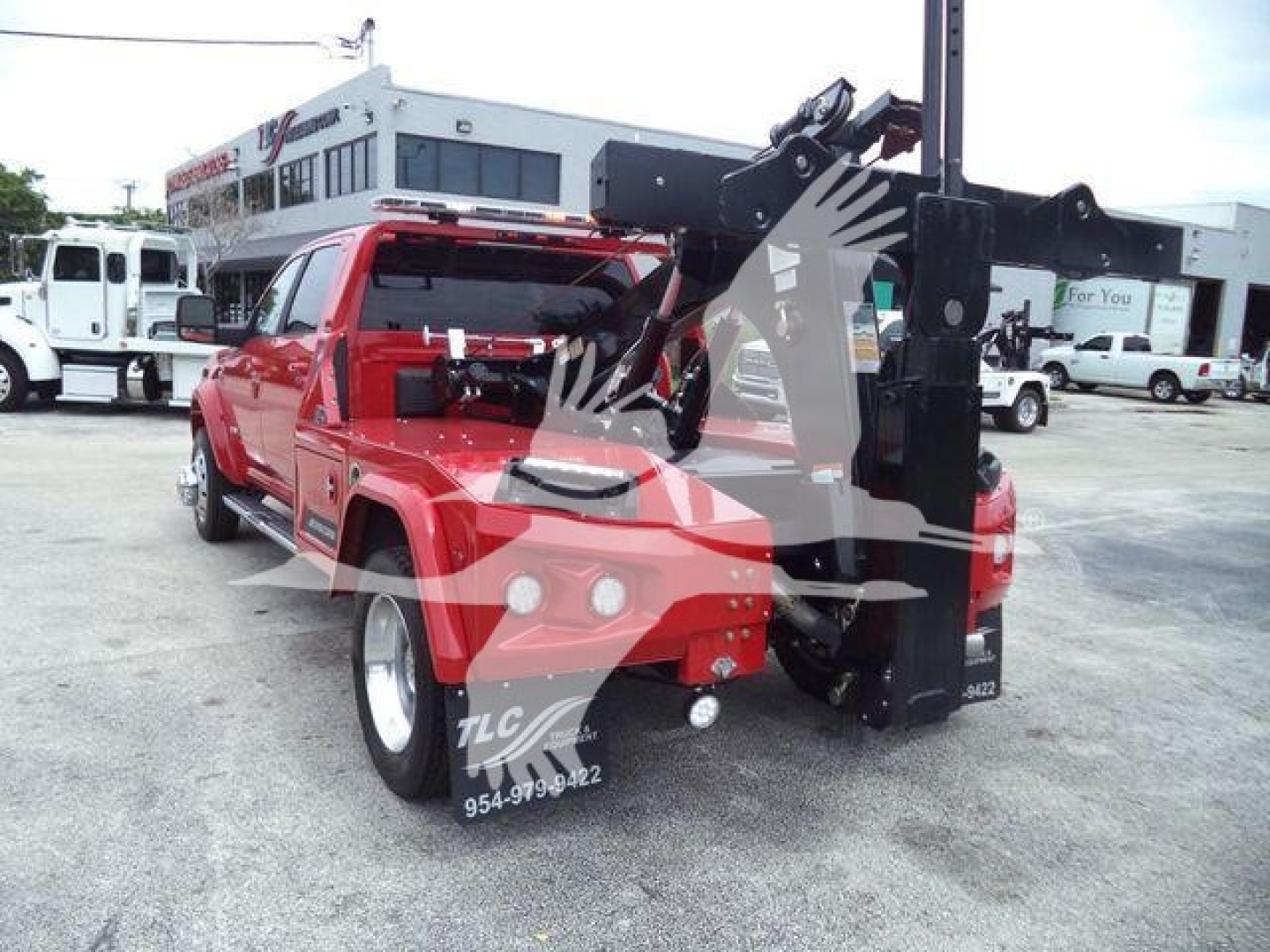 Truck bed with a large black hydraulic crane/winch assembly at rear, red Ram truck, dealership lot in background.