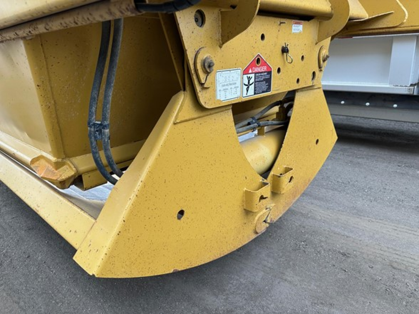 Bottom-dump trailer chassis in yellow showing structural frame and warning decals. Close-up of lower rear support with hydraulic components and safety labels visible.