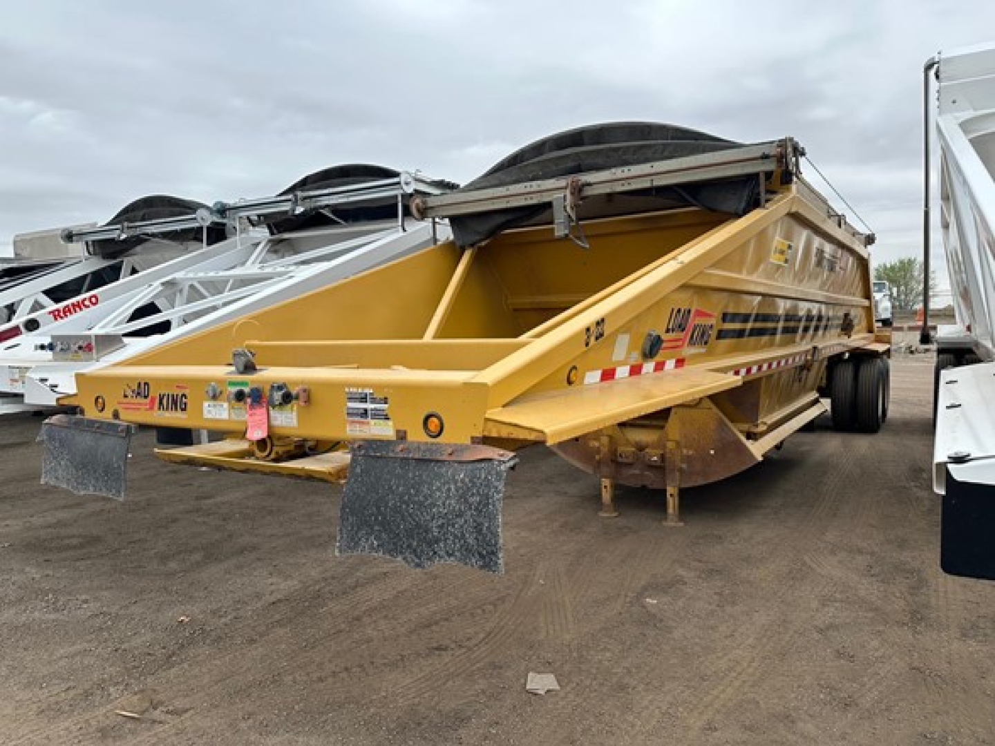 Bottom dump trailer showing Load King originator with yellow body and black tarp, rear view, mud flaps and reflective decals.