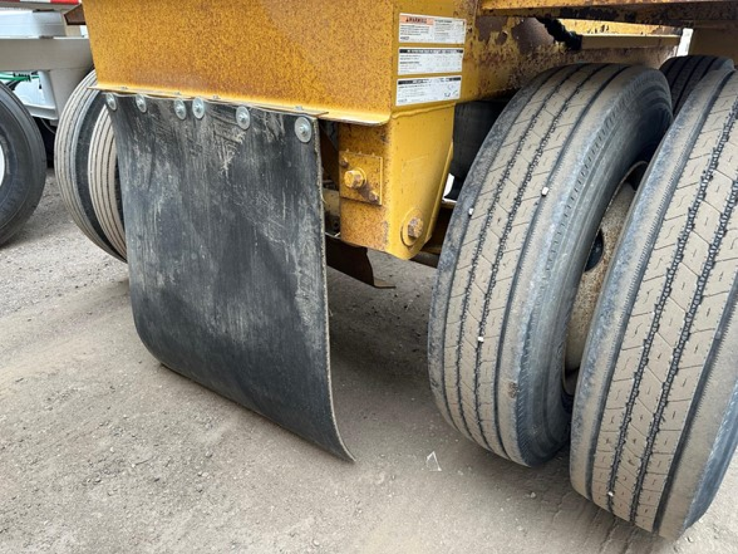Bottom-dump trailer with Load King originator design showing black blade/rear skirt and dual rear wheels on a rusted yellow chassis.