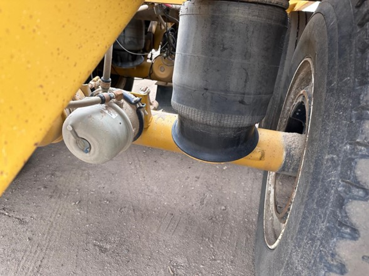 Bottom dump trailer ride side showing air tank and cylindrical component with hoses and painted yellow frame.