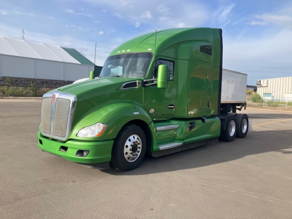 Green Kenworth T680 semi-truck in a parking lot, front three-quarter view.