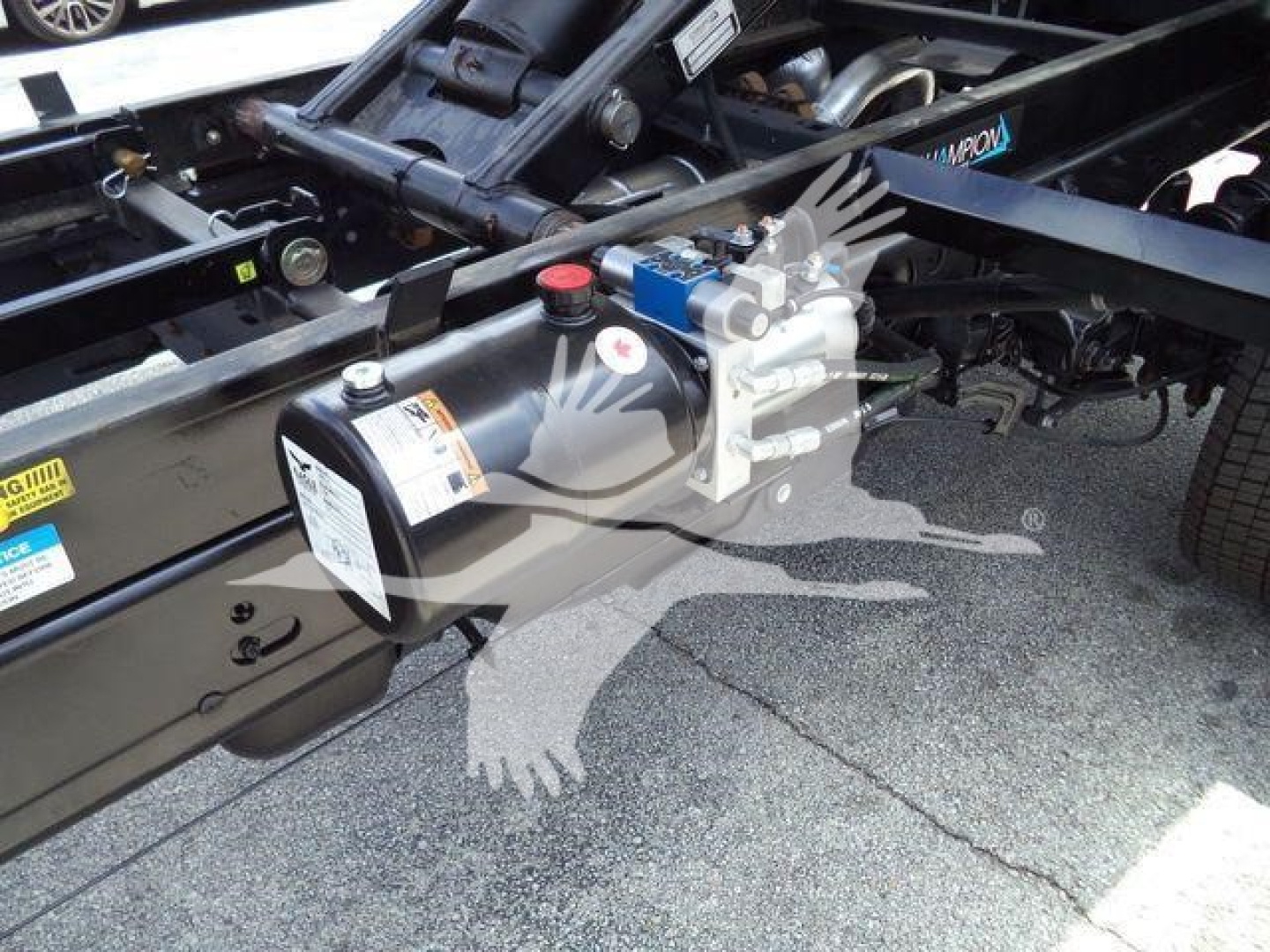 Ford F-550 chassis with air tank, hydraulic/air system mounted on frame; warning labels and pipes visible; components include a cylindrical air tank with warning label and a blue valve.