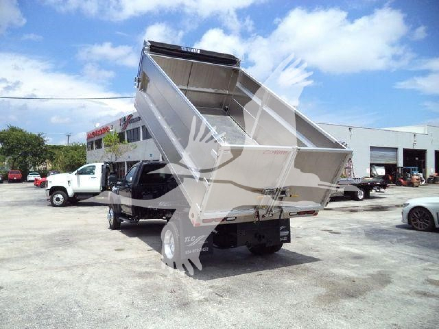Ford F-550 dump bed truck with bed raised, rear view showing dump box and tailgate; visible dealership lot in background with other vehicles.