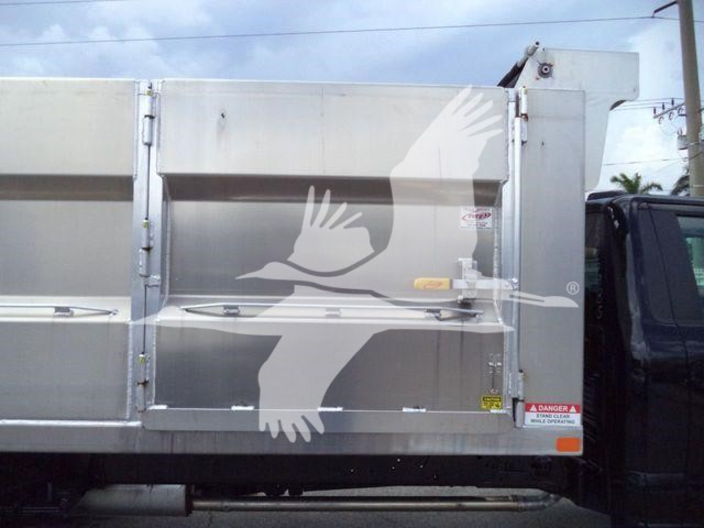 Ford F550 dump truck side view showing aluminum bed and safety decals with a white bird graphic on the side.
