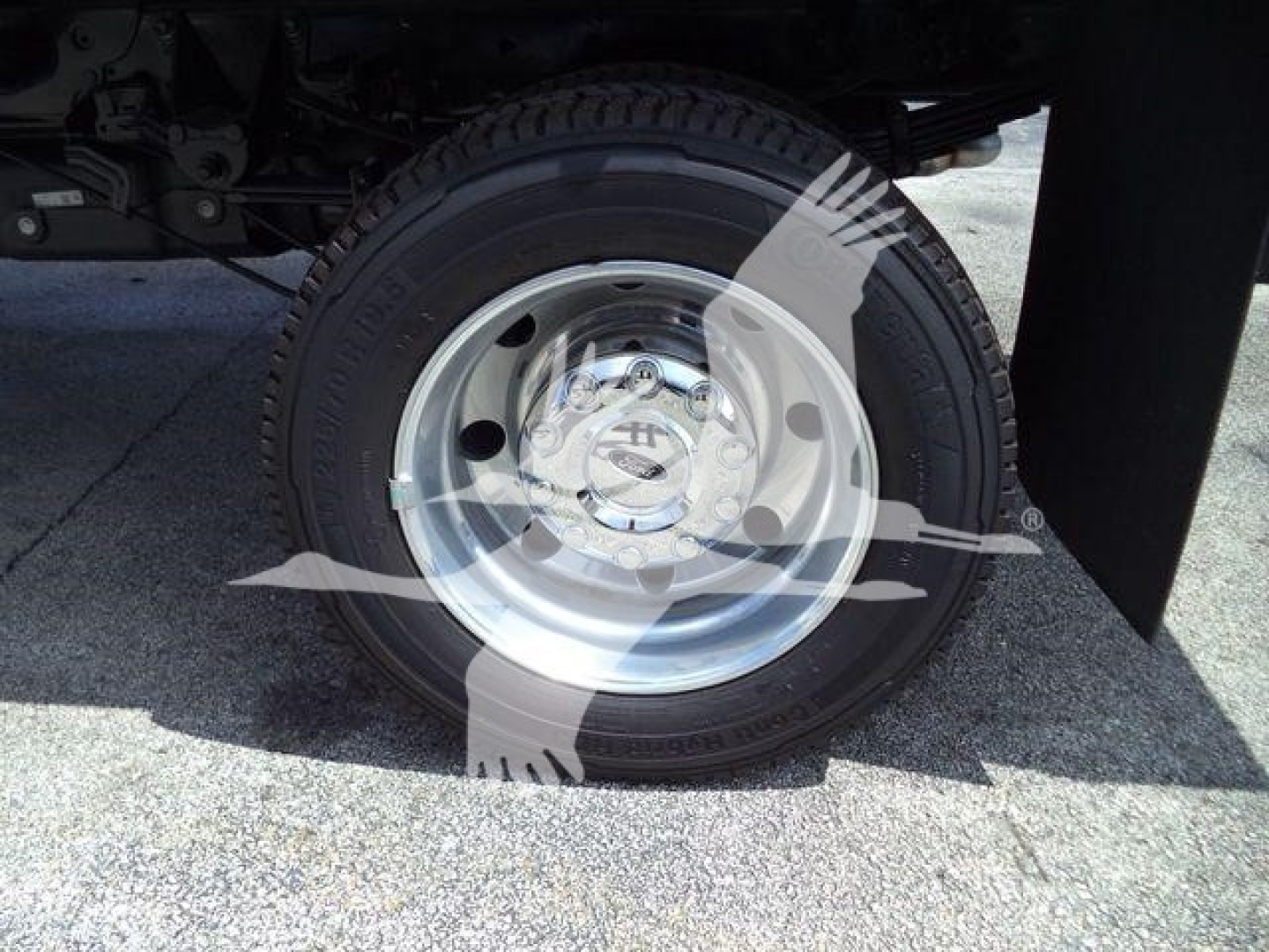Wheel and tire on Ford F-550 with hubcap and visible bolt pattern; partial undercarriage and fender, reflecting light on polished rim.