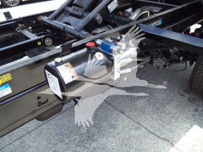 Ford F-550 chassis with air tank, hydraulic/air system mounted on frame; warning labels and pipes visible; components include a cylindrical air tank with warning label and a blue valve.