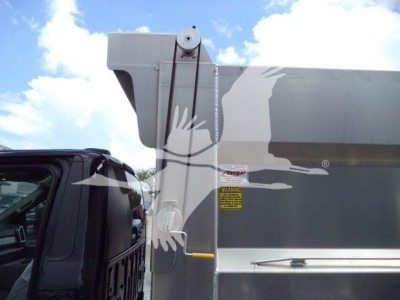 Ford F-550 dump bed side with warning label and hydraulic mechanism visible; silver body with yellow latch and black cab window.