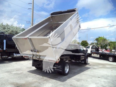 Dump bed on a Ford F-550 dump truck in raised position, two front wheels visible, black chassis, light silver dump bed, dealership lot in background.
