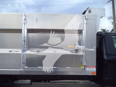Ford F550 dump truck side view showing aluminum bed and safety decals with a white bird graphic on the side.