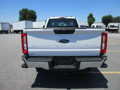 Ford Super Duty tailgate of a white 2026 F-250 showing 'SUPER DUTY' lettering, Ford logo, rear bumper with step pads, tail lights, and hitch receiver.