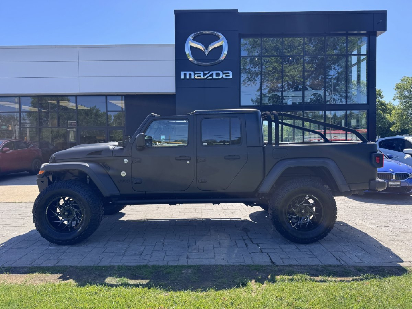 2020 Jeep Gladiator four-door pickup truck in front of Mazda showroom with large off-road tires and lifted suspension.