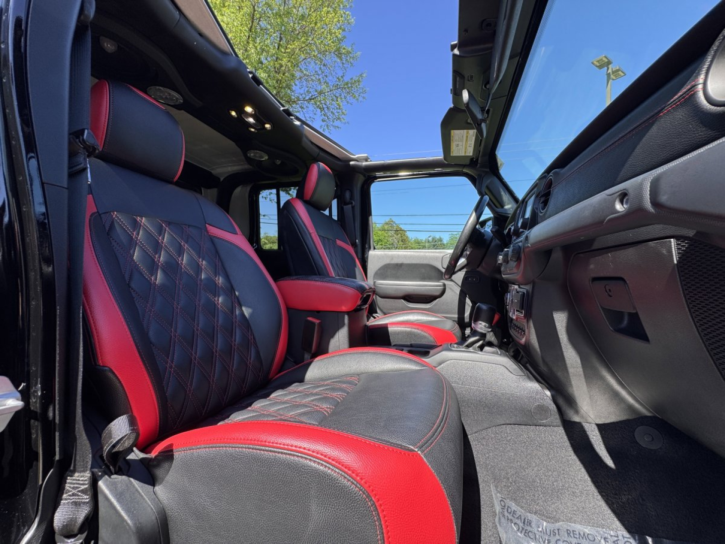 Jeep Gladiator interior view showing front seats with red and black leather upholstery, open roof, and dashboard from the passenger side.
