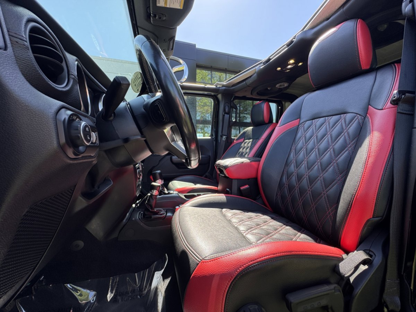 Jeep Gladiator interior showing front seat with red and black diamond-stitched upholstery and steering wheel in view.