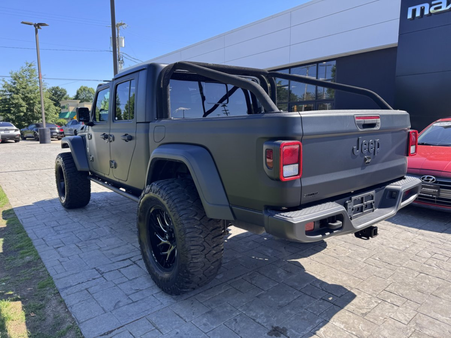 Jeep Gladiator rear three-quarter view with aftermarket roll cage and large off-road tires.