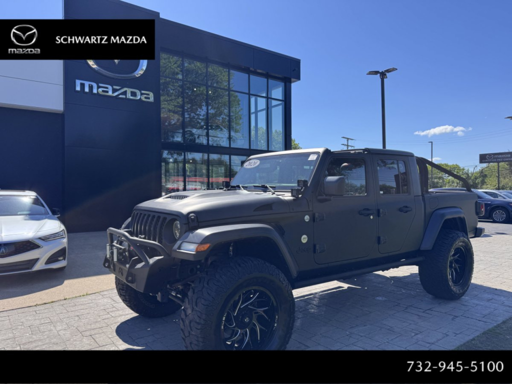 Jeep Gladiator pickup truck in dark color with aftermarket front bumper and lifted tires in dealership lot.