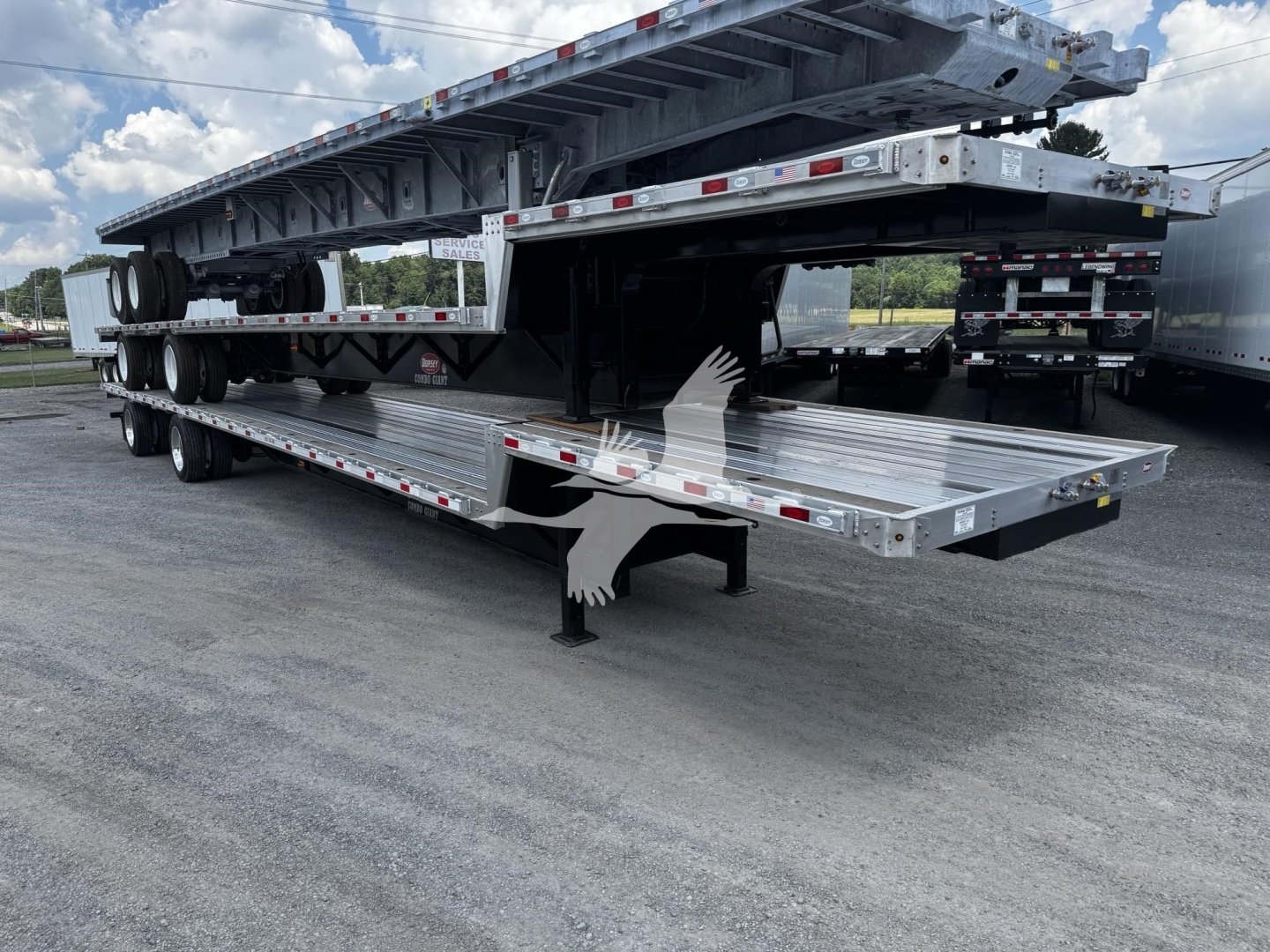 Trailer with stacked flatbed sections and a ramp, showing multiple axles and a detachable gooseneck.