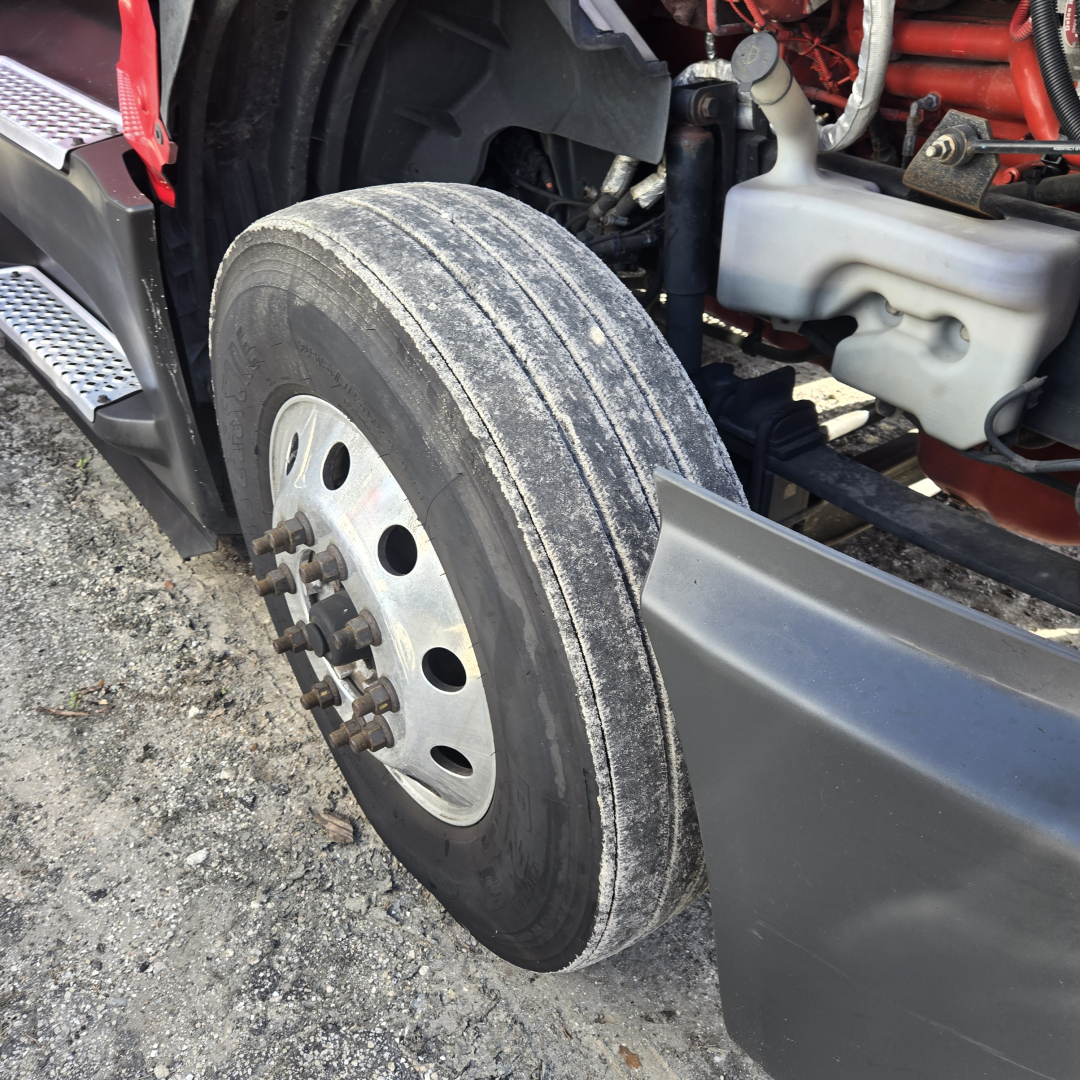 Truck front wheel with exposed dual-stack air horn and part of engine bay; visible tire tread and steel wheel with lug nuts; lower fender and side step.
