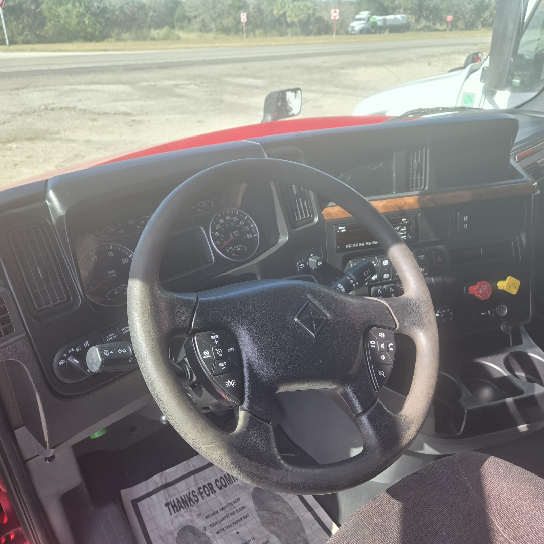 Truck cab interior of a 2020 International LT625 mid-roof showing steering wheel with controls, dashboard gauges, and center console
