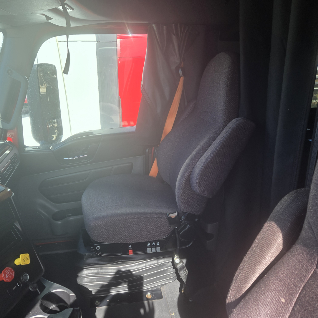 Interior cab view of a 2020 International LT625 midroof truck showing driver seat and passenger seat, with a black curtain between sleeper area and cab.