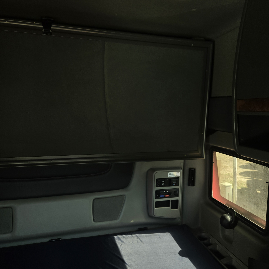 Truck cab interior panel and window area showing overhead bunk cabinet and side control panel.