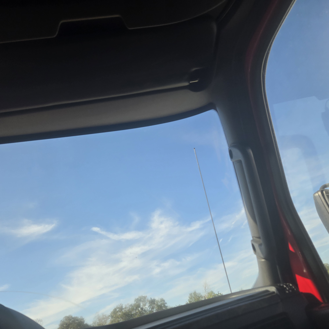 Truck cab interior window view with blue sky, hint of door pillar and window frame.