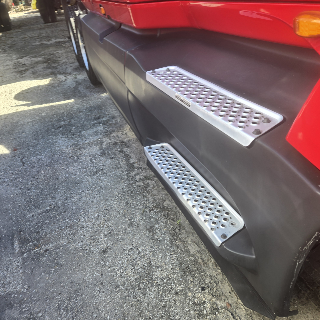 Truck side view showing shiny perforated metal steps along with black body panel and red cab of a 2020 International LT625 midroof.