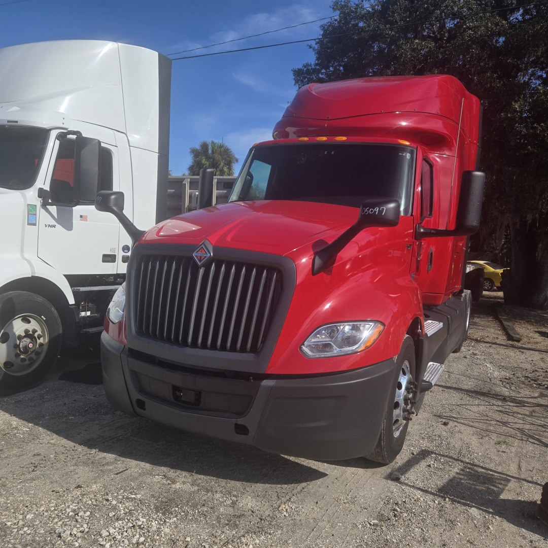2020 International LT625 midroof sleeper cab tractor showing bright red exterior, front grille, headlights, and side mirrors; other white truck in background.