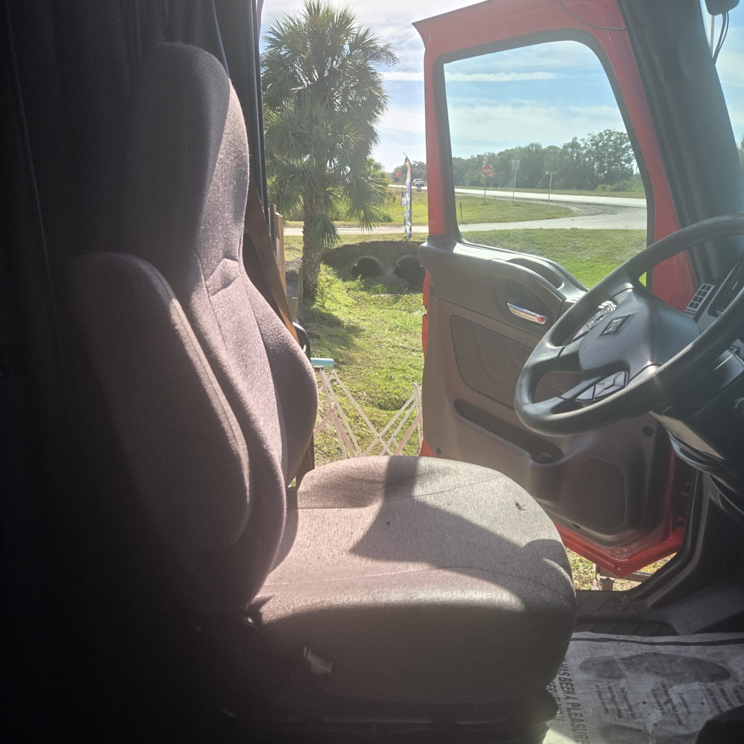 Truck cab interior showing driver seat and steering wheel in a red International LT625 MIDROOF truck.