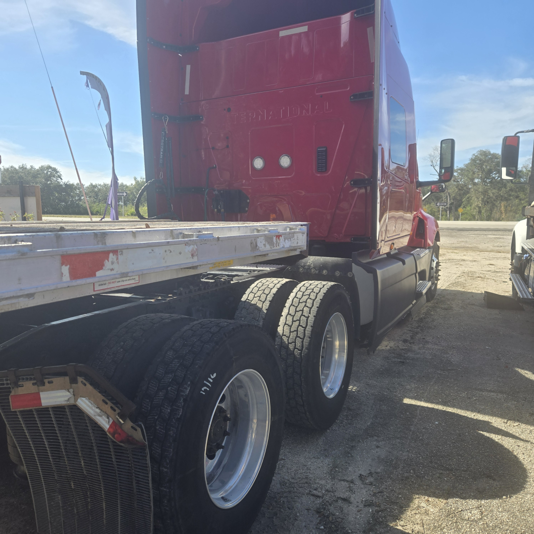 Truck cab rear and side showing International LT625 midroof sleeper with triple rear wheels and a flatbed trailer chassis.