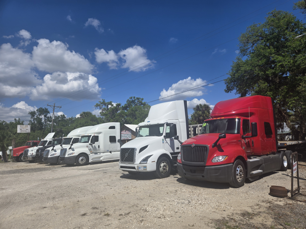 Trucks in a row: white and red semi-trucks parked at a lot with a bright blue sky.