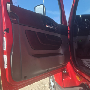 Truck door panel inside cab of a red 2020 International LT625 midroof showing interior door panel and part of dashboard.