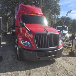 Truck cab front view of a red 2020 International LT625 Midroof, with large vertical grille, black bumper, and side mirrors.