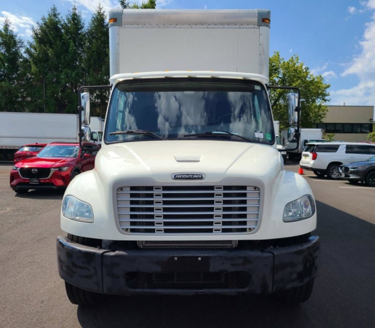 Freightliner M2 106 medium-duty box truck front view showing large grille, headlights, white cab, and box cargo area.