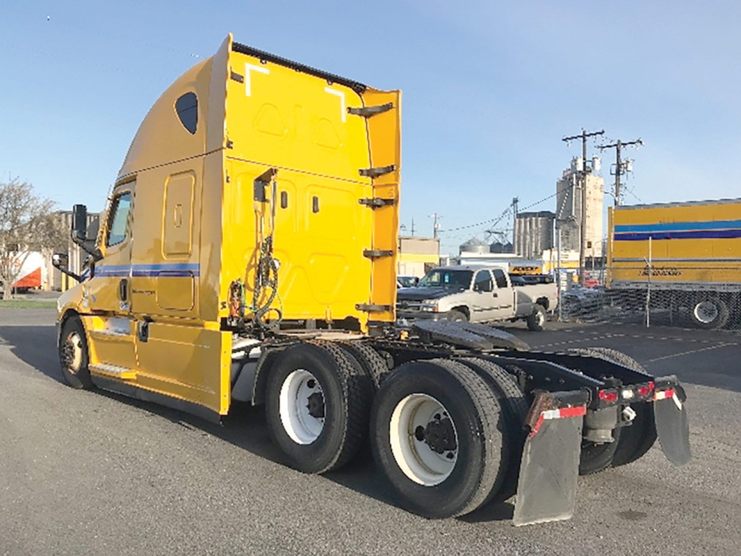Yellow Freightliner Cascadia126 tractor cab rear/side view showing sleeper, fuel lines, and dual rear axles with mud flaps; no legible text visible on the image itself.