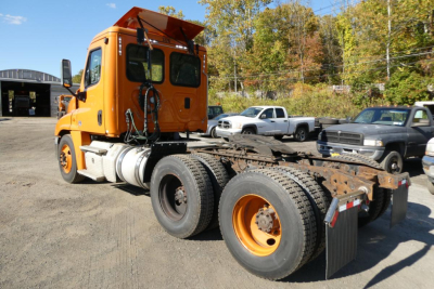 Orange Freightliner Cascadia 125 daytime cab rear view showing chassis and wheelset with dual rear axles and fifth wheel mount.