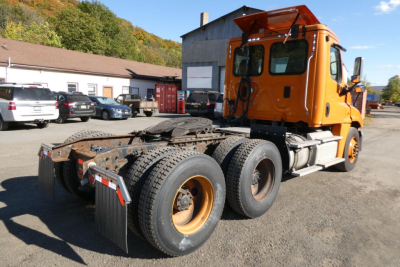 Truck chassis and cab of a Freightliner Cascadia 125 tractor viewed from rear side showing orange cab and dual rear axles with tires.