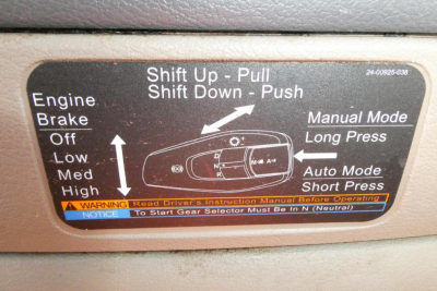 Panel showing shift control instructions in Freightliner Cascadia cab: 'Shift Up - Pull, Shift Down - Push' with diagram of gear lever, manual mode, auto mode and warning text.