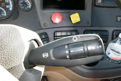 Steering column stalks in a Freightliner Cascadia truck showing drive mode controls with D N R letters, a leather textured dashboard, and gauge cluster in the background.