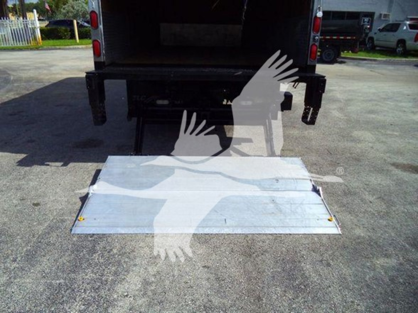 Isuzu NRR box truck rear with deployed aluminum ramp/dolly fold-down ramp. Tail area shows open cargo area and rear bumper hooks.