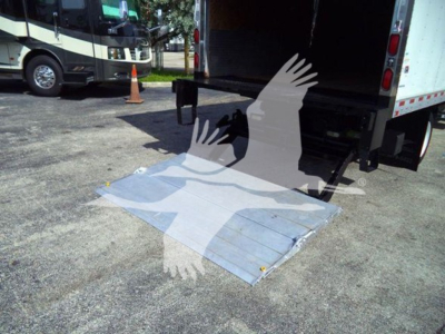 Isuzu NRR box truck rear with lowered aluminum ramp; ramp on ground; two other buses in background; open cargo area.
